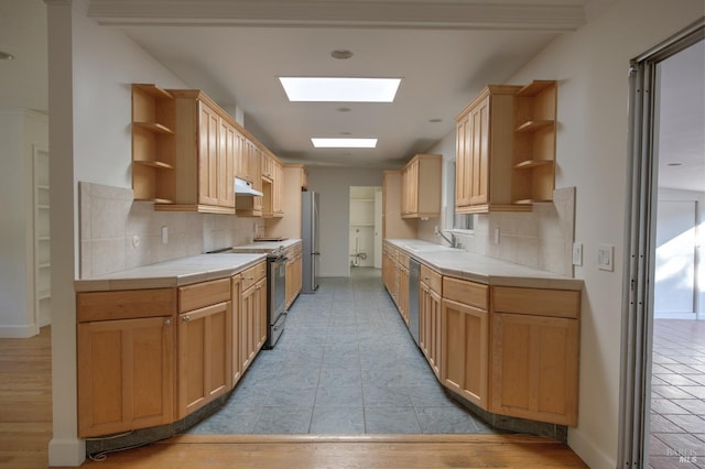 kitchen with appliances with stainless steel finishes, a skylight, sink, backsplash, and tile countertops