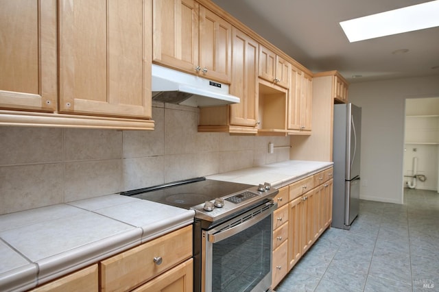 kitchen featuring a skylight, tile countertops, stainless steel appliances, tasteful backsplash, and light brown cabinetry