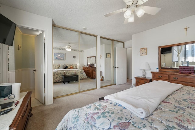 bedroom with ceiling fan, light colored carpet, a textured ceiling, and multiple closets