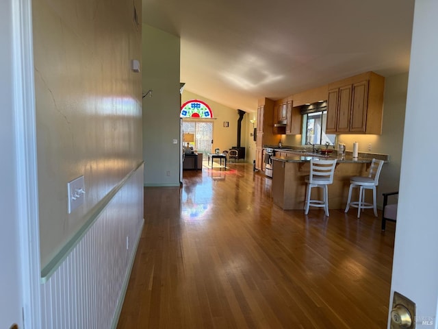 kitchen with lofted ceiling, dark wood-type flooring, stainless steel range with gas cooktop, kitchen peninsula, and a breakfast bar