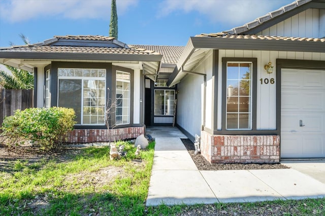 doorway to property featuring brick siding, a tile roof, and a garage