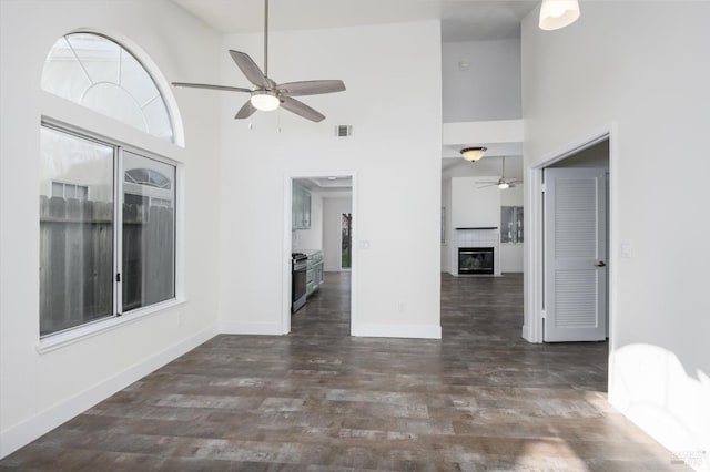 unfurnished living room featuring dark wood-type flooring, visible vents, a ceiling fan, and a towering ceiling