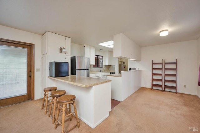 kitchen with tasteful backsplash, kitchen peninsula, stainless steel refrigerator, a breakfast bar area, and white cabinets