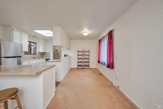 kitchen featuring white cabinetry, decorative backsplash, kitchen peninsula, stainless steel refrigerator, and a breakfast bar