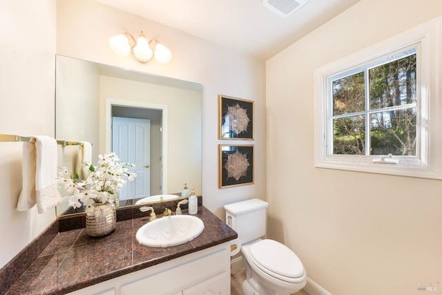 half bathroom featuring toilet, vanity, visible vents, and baseboards