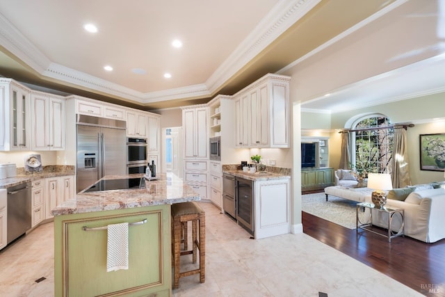 kitchen featuring ornamental molding, built in appliances, a kitchen island with sink, a tray ceiling, and open shelves