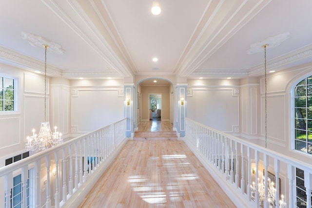 corridor featuring arched walkways, a chandelier, a wealth of natural light, and a decorative wall