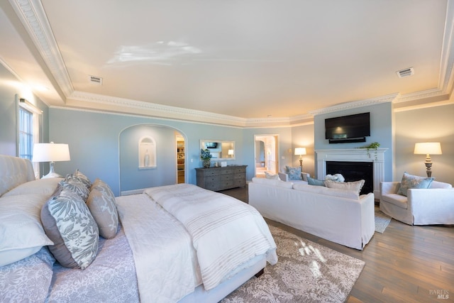 bedroom featuring arched walkways, a fireplace, crown molding, visible vents, and wood finished floors