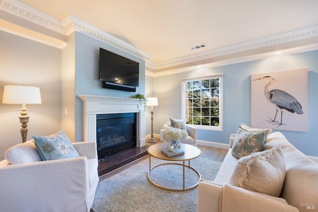 living room featuring crown molding, visible vents, a glass covered fireplace, wood finished floors, and baseboards