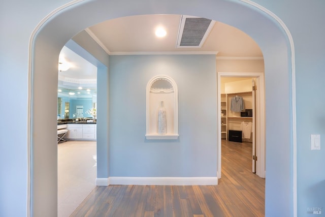 hall featuring arched walkways, crown molding, visible vents, wood finished floors, and baseboards