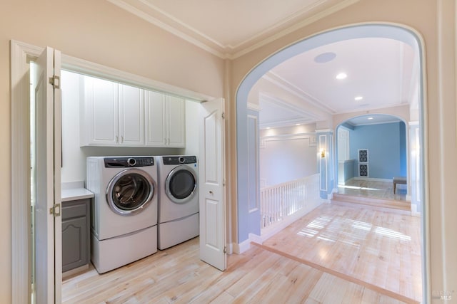 washroom with arched walkways, crown molding, light wood finished floors, cabinet space, and separate washer and dryer