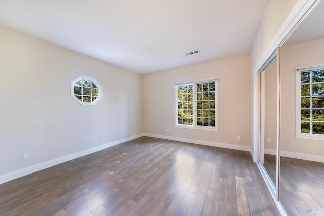 unfurnished bedroom with dark wood-type flooring, multiple windows, visible vents, and baseboards