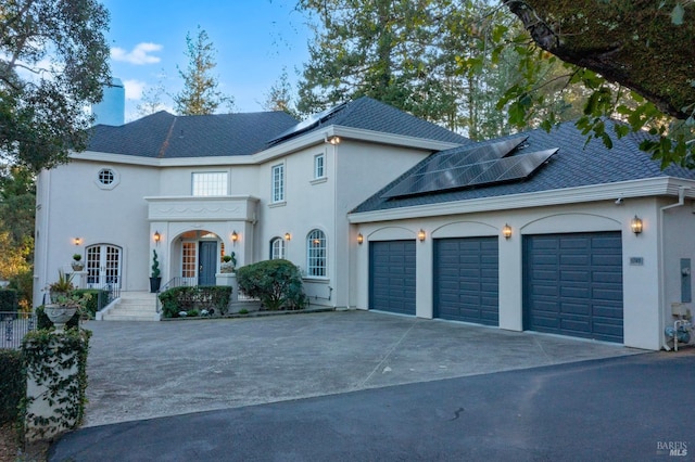 view of front facade featuring a garage, solar panels, a shingled roof, concrete driveway, and french doors