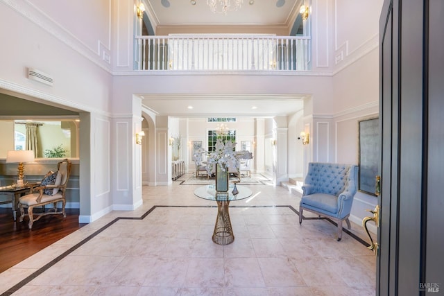 entrance foyer featuring ornate columns, crown molding, a decorative wall, and a notable chandelier