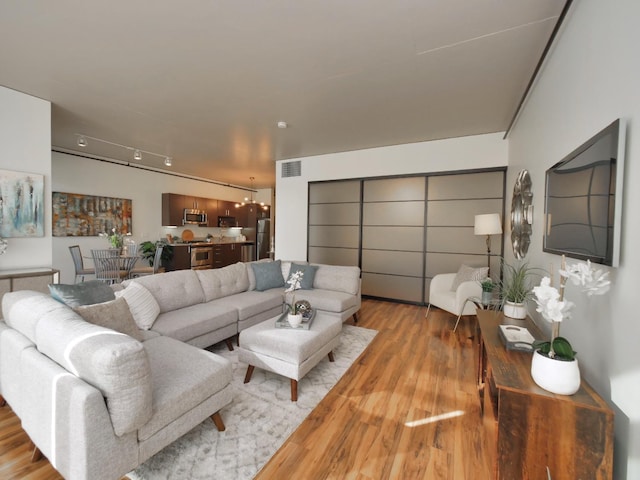 living room with track lighting, light wood-style floors, and visible vents