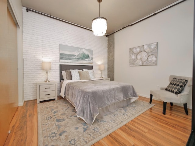 bedroom with brick wall, an inviting chandelier, and light hardwood / wood-style flooring