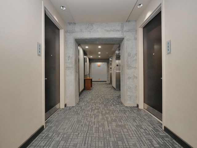 hallway featuring elevator, baseboards, and carpet