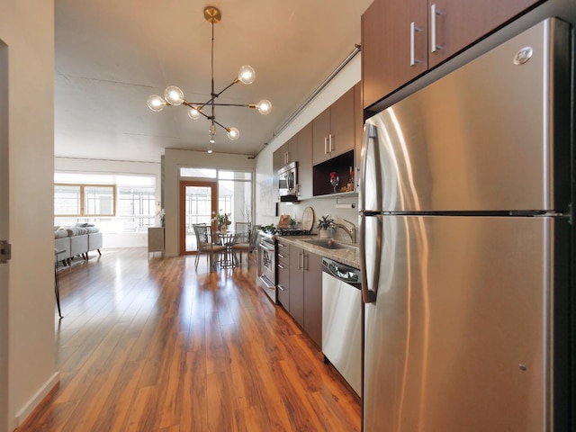 kitchen with a sink, a notable chandelier, wood finished floors, and stainless steel appliances