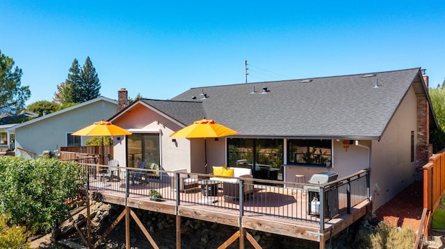 back of property with stucco siding, a wooden deck, a chimney, and roof with shingles