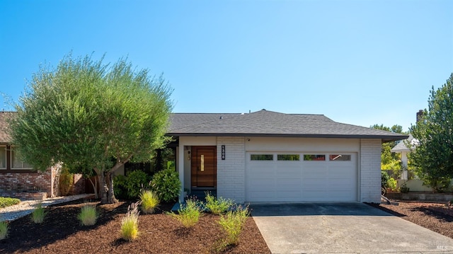 view of front facade featuring an attached garage, roof with shingles, concrete driveway, and brick siding