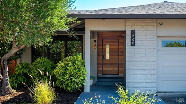 entrance to property featuring roof with shingles, brick siding, and an attached garage