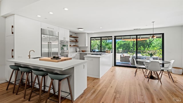 kitchen with a breakfast bar, stainless steel appliances, light countertops, light wood-style floors, and a peninsula