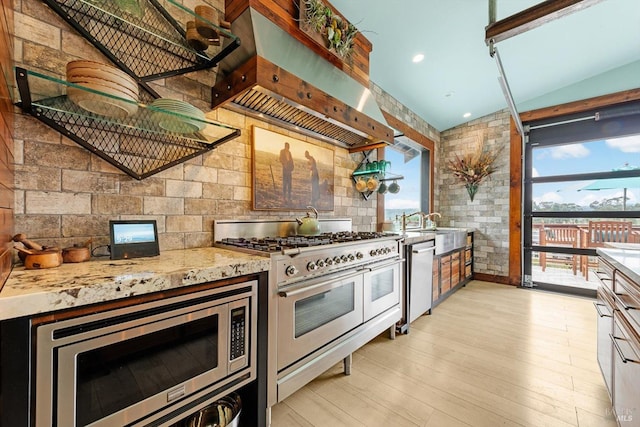 kitchen with range hood, light wood finished floors, appliances with stainless steel finishes, vaulted ceiling, and light stone countertops