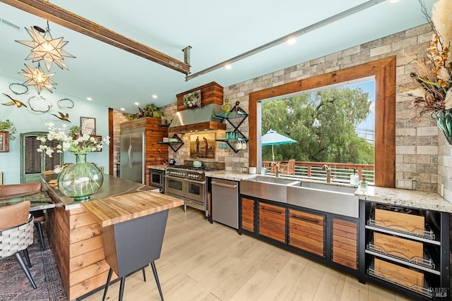 kitchen featuring premium appliances, recessed lighting, wood counters, wall chimney range hood, and light wood-type flooring