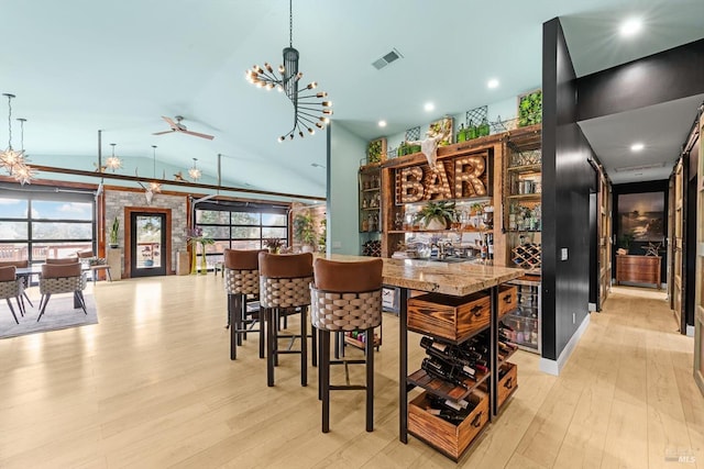 bar with a dry bar, visible vents, a ceiling fan, vaulted ceiling, and wood finished floors