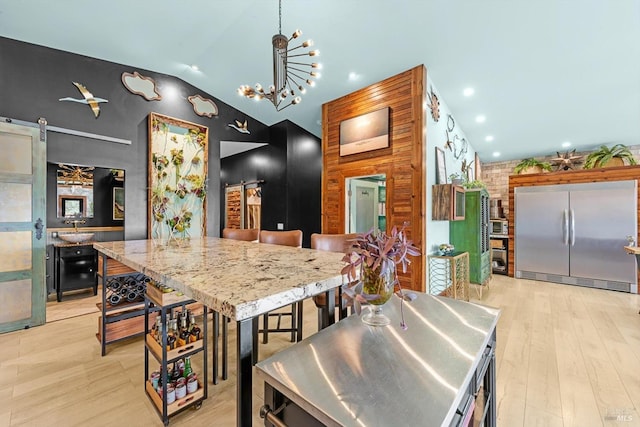 kitchen featuring light wood finished floors, lofted ceiling, recessed lighting, a barn door, and built in refrigerator