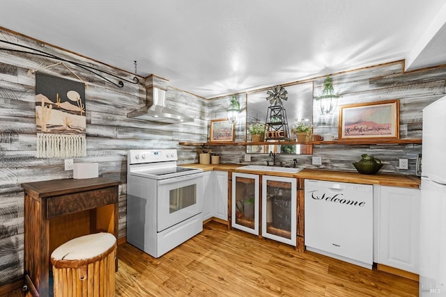 kitchen featuring wooden counters, light wood-style floors, a sink, wall chimney range hood, and white appliances