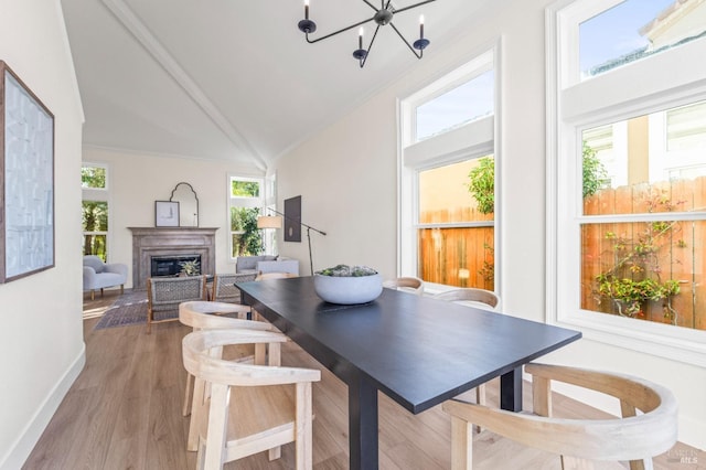 dining area with a fireplace, light wood finished floors, lofted ceiling, an inviting chandelier, and baseboards