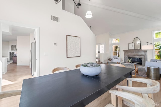 dining room featuring high vaulted ceiling, a high end fireplace, visible vents, and light wood-style flooring