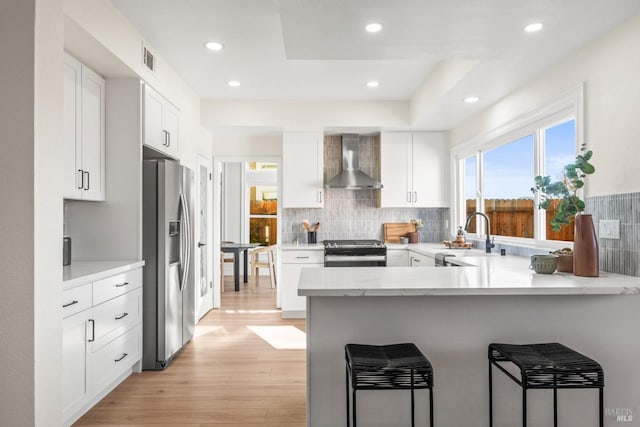 kitchen with a peninsula, white cabinets, light countertops, appliances with stainless steel finishes, and wall chimney exhaust hood