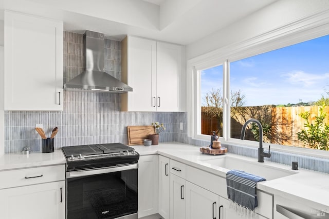 kitchen featuring stainless steel gas stove, wall chimney exhaust hood, white cabinetry, and decorative backsplash