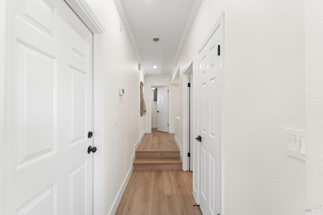 corridor featuring crown molding, light wood-style flooring, and baseboards