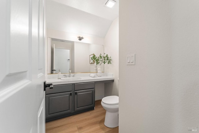 half bathroom featuring lofted ceiling, toilet, wood finished floors, and vanity