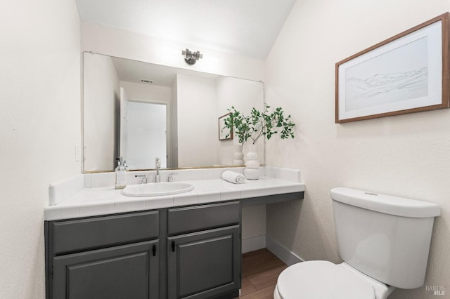 bathroom with toilet, vaulted ceiling, vanity, wood finished floors, and baseboards