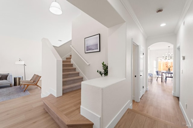 corridor featuring ornamental molding, arched walkways, light wood finished floors, and stairs