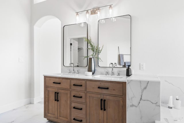 full bath featuring double vanity, marble finish floor, baseboards, and a sink