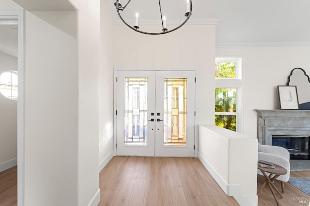 entryway featuring light wood finished floors, baseboards, crown molding, french doors, and a fireplace