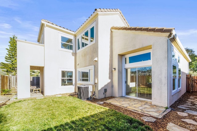 rear view of house with a tile roof, stucco siding, central air condition unit, a lawn, and fence