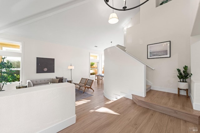 living area featuring high vaulted ceiling, baseboards, stairs, light wood-type flooring, and beam ceiling