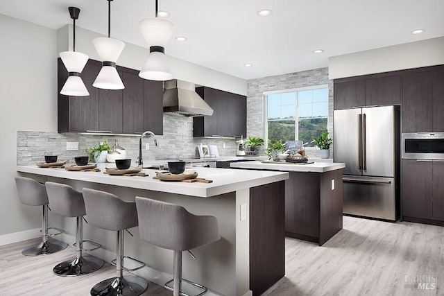 kitchen featuring stainless steel fridge, wall oven, decorative light fixtures, a kitchen island, and wall chimney exhaust hood