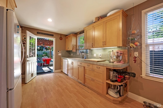 kitchen with tile counters, backsplash, white appliances, light hardwood / wood-style flooring, and sink