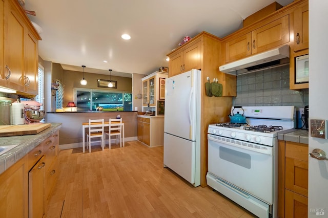 kitchen with tile countertops, tasteful backsplash, decorative light fixtures, white appliances, and light hardwood / wood-style flooring