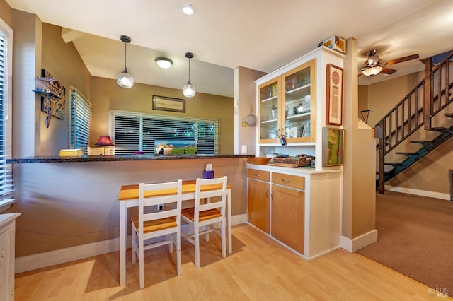 kitchen featuring decorative light fixtures, a kitchen breakfast bar, kitchen peninsula, ceiling fan, and light hardwood / wood-style flooring