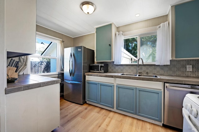 kitchen featuring tile countertops, stainless steel appliances, decorative backsplash, light hardwood / wood-style flooring, and sink