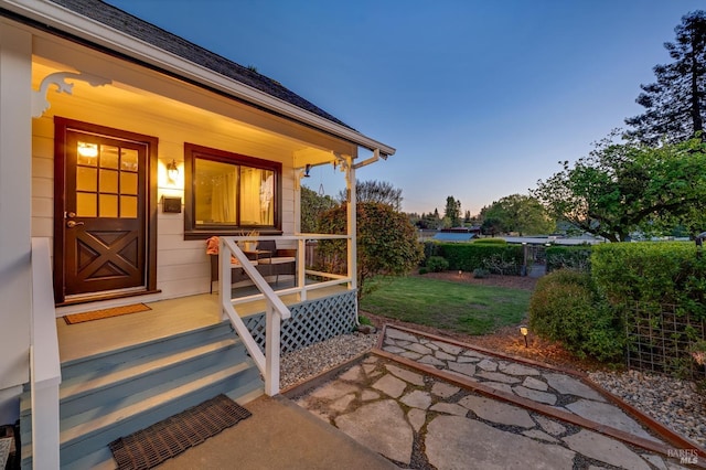 exterior entry at dusk featuring covered porch and a yard