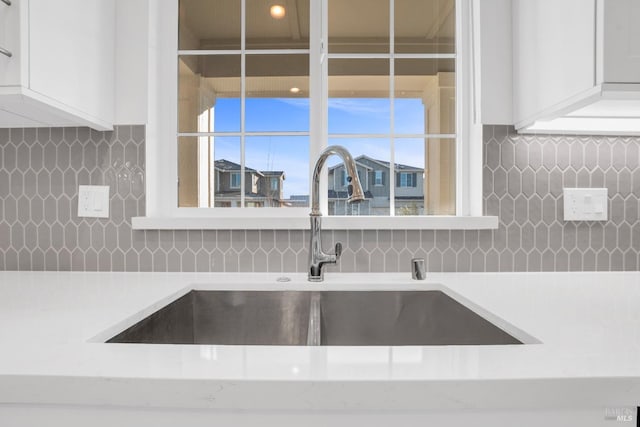 interior details with tasteful backsplash, sink, and white cabinetry